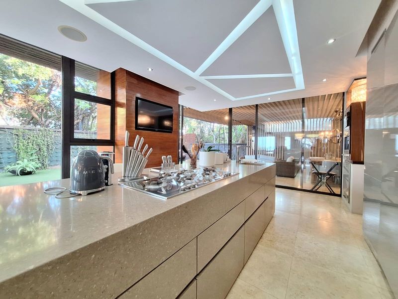 Modern kitchen featuring a large stone island with integrated gas cooktop, wood-paneled accents, and floor-to-ceiling glass walls overlooking the garden.