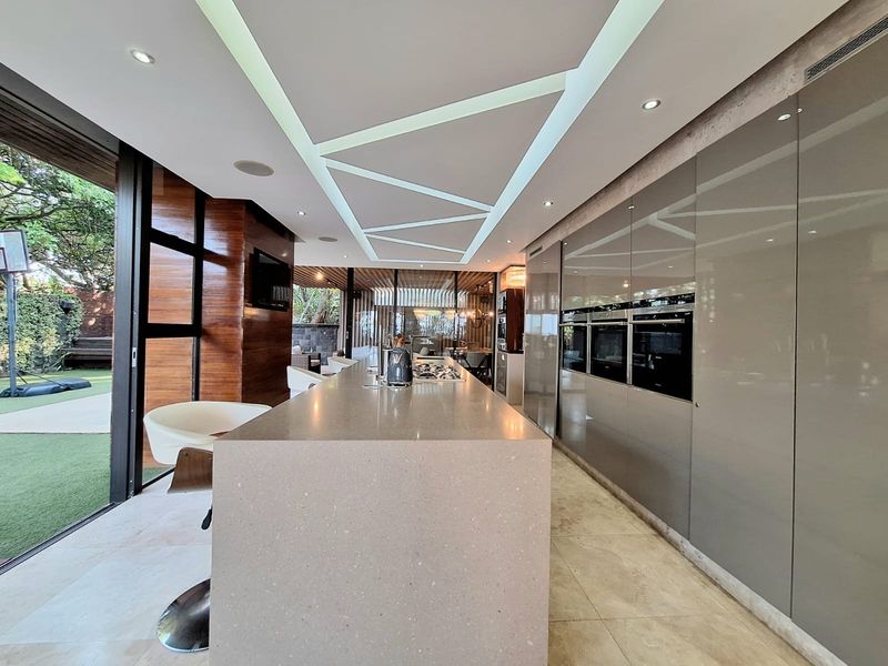 Modern kitchen featuring a large stone island, integrated high-end appliances, sleek cabinetry, and expansive sliding glass doors opening to the outdoor area.