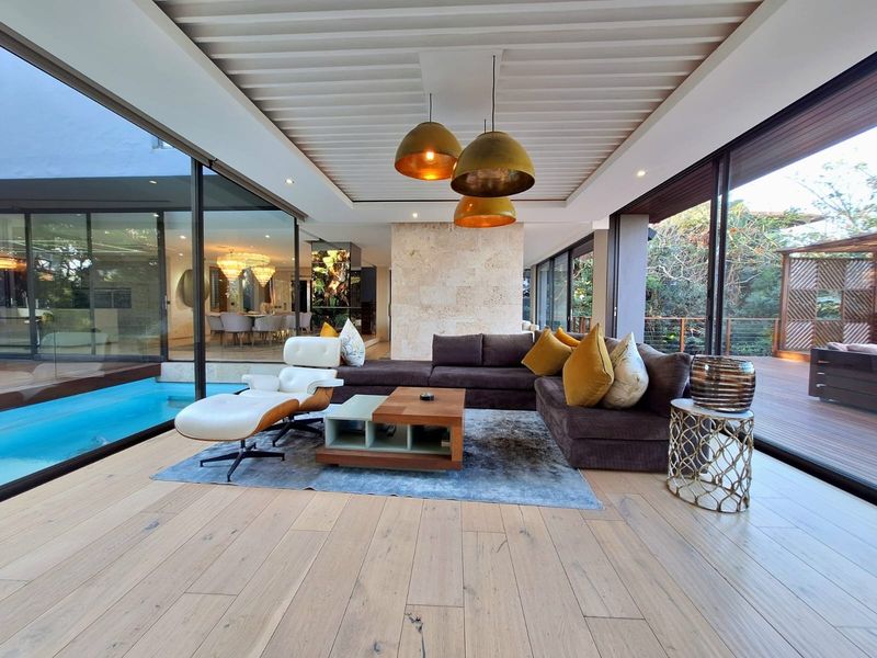 Spacious modern living area featuring timber flooring, a stone feature wall, and expansive floor-to-ceiling glass doors opening to a pool and deck.