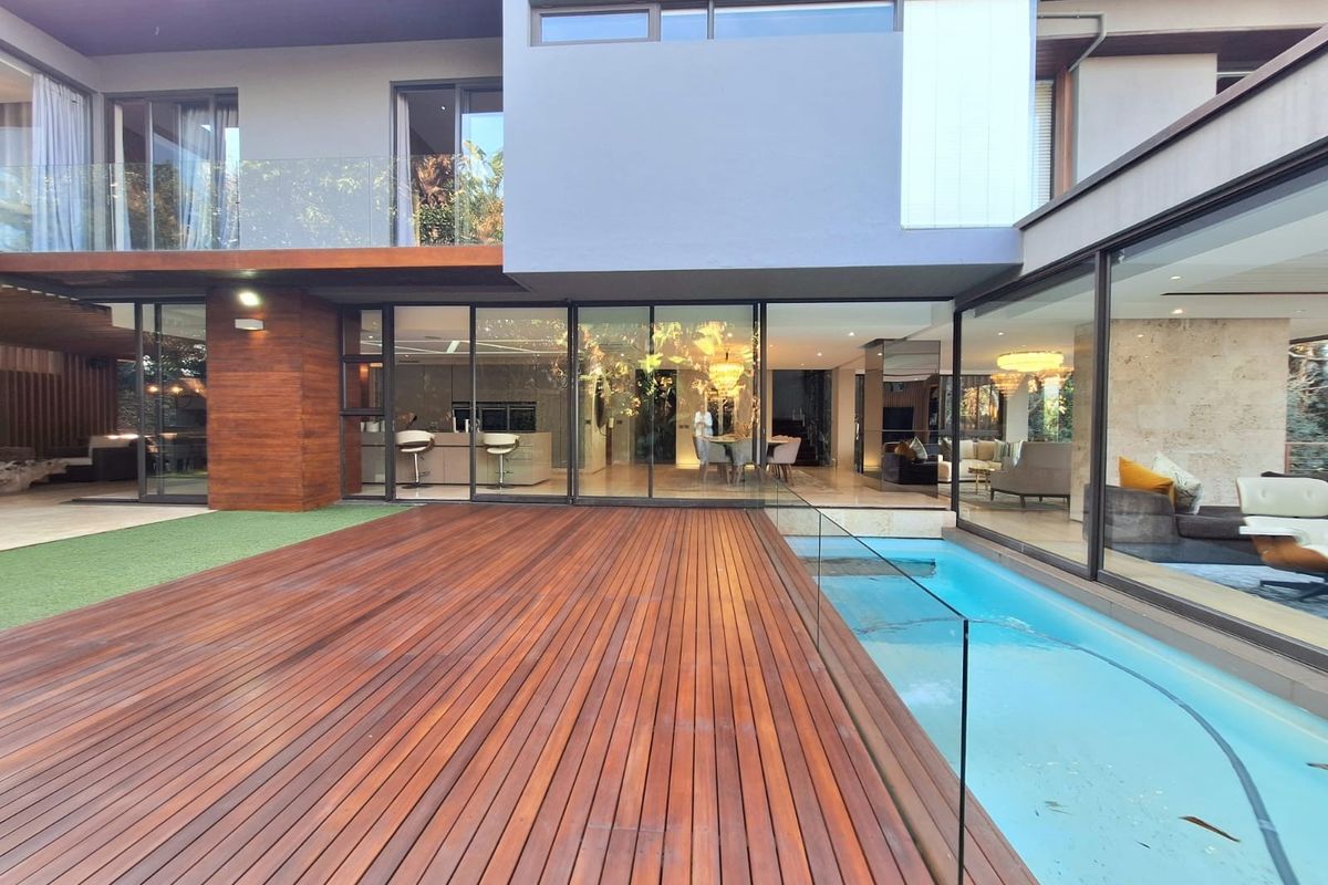 Modern rear exterior featuring a timber deck, glass balustrade, and swimming pool, seamlessly connecting to the open-plan interior through large sliding glass doors.