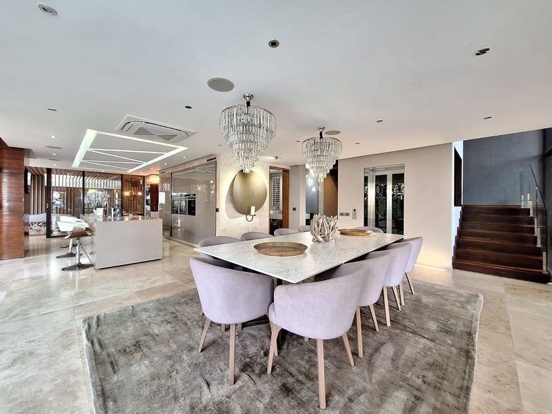 Spacious open-plan living and dining area featuring a modern kitchen island, stone flooring, and a striking timber staircase with glass balustrade.