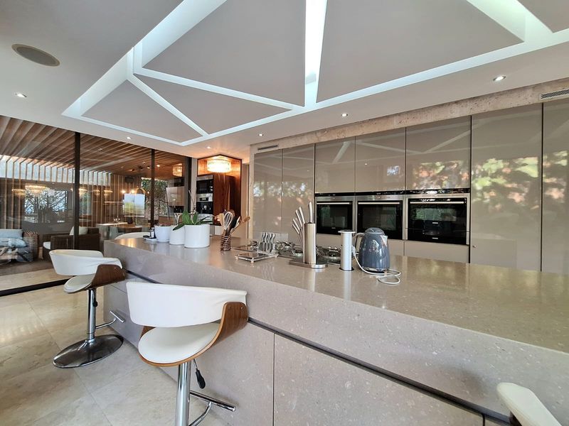 Modern luxury kitchen featuring a large stone island, integrated triple ovens, and sophisticated recessed ceiling lighting with seamless flow to outdoor living areas.