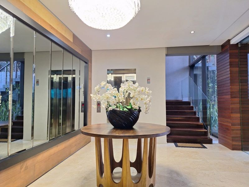 Elegant entrance foyer featuring stone flooring, timber wall paneling, a modern elevator, and a striking timber staircase with glass balustrades.