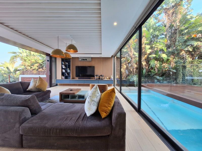 Modern open-plan living area featuring slatted timber ceilings, custom wall paneling, and expansive floor-to-ceiling glass doors opening directly onto a private pool deck.