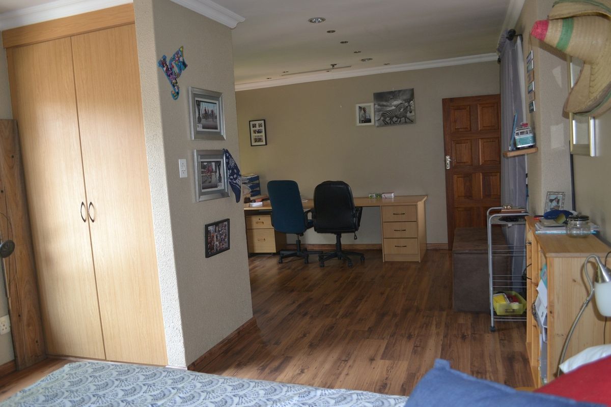 A bedroom featuring built-in wooden cabinetry and laminate flooring, with an adjoining study area visible through the open-plan layout.