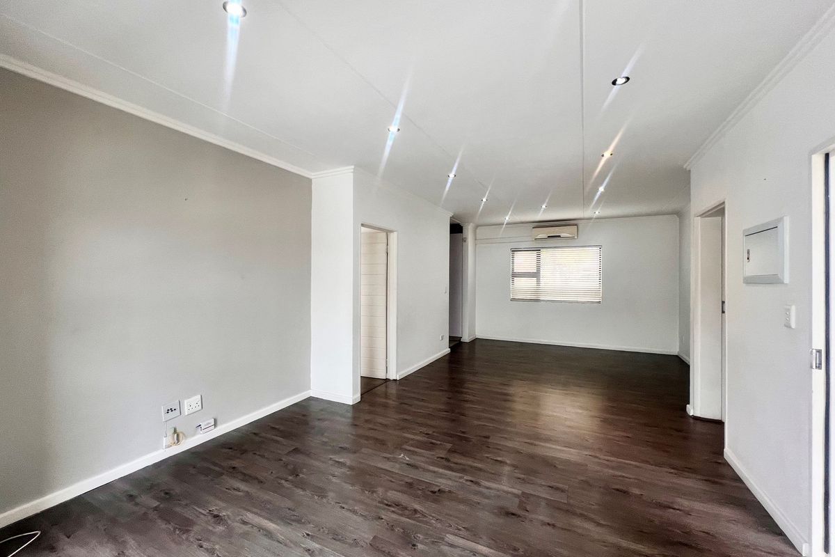 Spacious living area featuring dark wood-look flooring, recessed ceiling downlights, and a wall-mounted air conditioning unit.