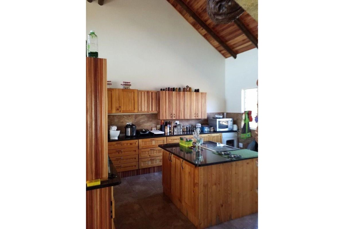 A kitchen featuring wooden cabinetry, a central island with a dark countertop, and a high vaulted timber-beamed ceiling.