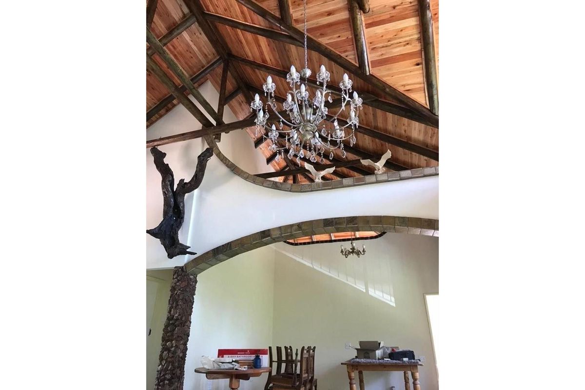 Spacious living area featuring a high vaulted timber ceiling with exposed beams, a decorative stone-clad archway, and a large crystal chandelier.