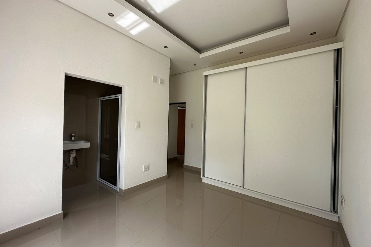 A bright bedroom featuring tiled flooring, a built-in sliding door wardrobe, and an en-suite bathroom with a modern vanity and shower.