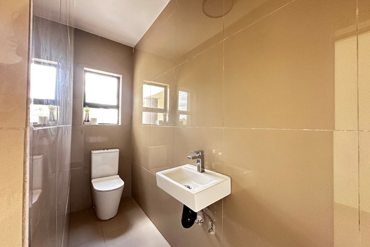 A compact guest bathroom featuring modern wall-mounted basin, sleek chrome tapware, and floor-to-ceiling neutral tiling.