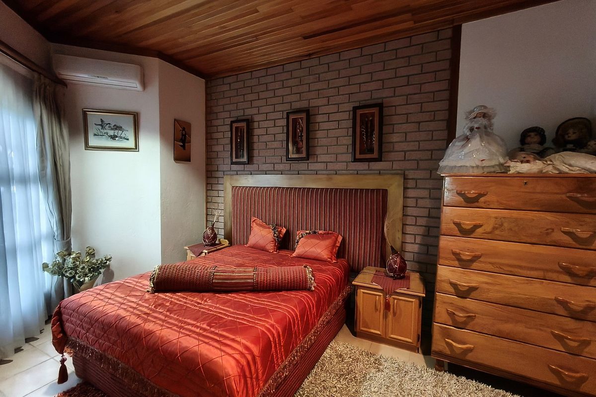 A bedroom featuring a distinctive exposed brick feature wall, timber-paneled ceiling, and a wall-mounted air conditioning unit.
