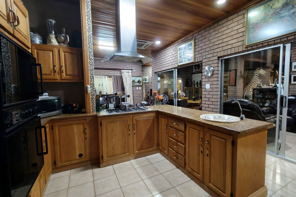 A spacious kitchen featuring timber cabinetry, granite countertops, a built-in oven, and a stainless steel extractor fan, with an open-plan layout.