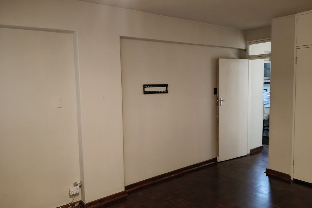 An empty living area featuring dark parquet flooring, built-in storage cupboards, and a wall-mounted television bracket, requiring minor cosmetic updates.