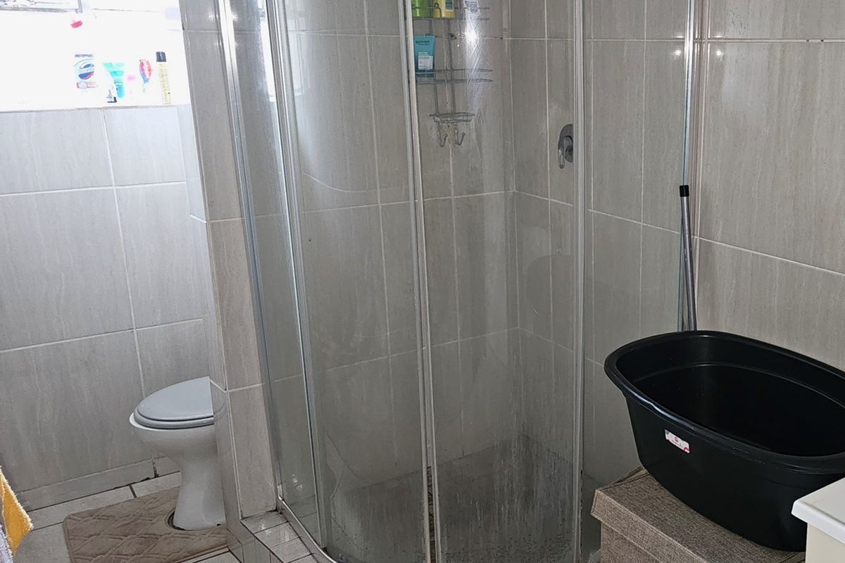 A functional bathroom featuring a glass shower enclosure and a standard toilet with neutral wall and floor tiling.