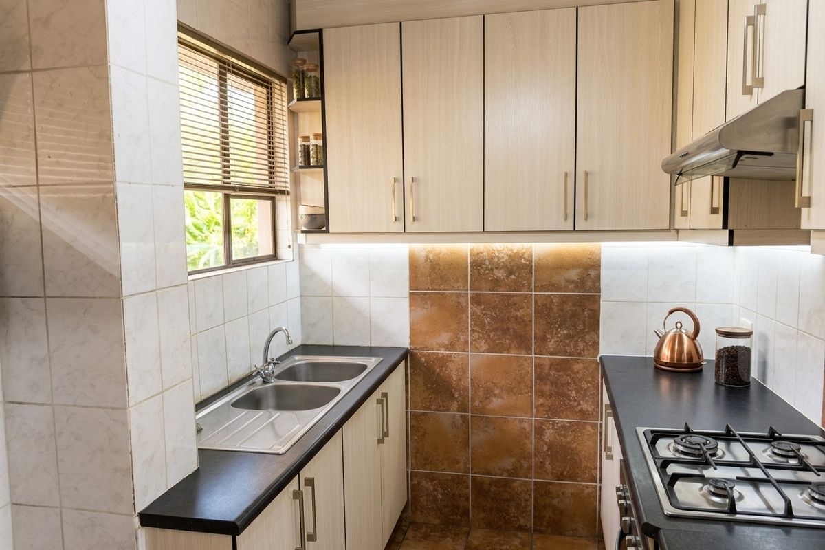 A well-maintained kitchen featuring light wood cabinetry, dark countertops, a double basin sink, gas hob, and integrated extractor fan with under-cabinet lighting.