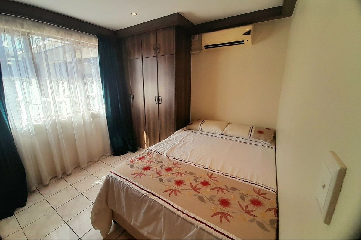 A bedroom featuring built-in wooden cupboards, tiled flooring, and a wall-mounted air conditioning unit.