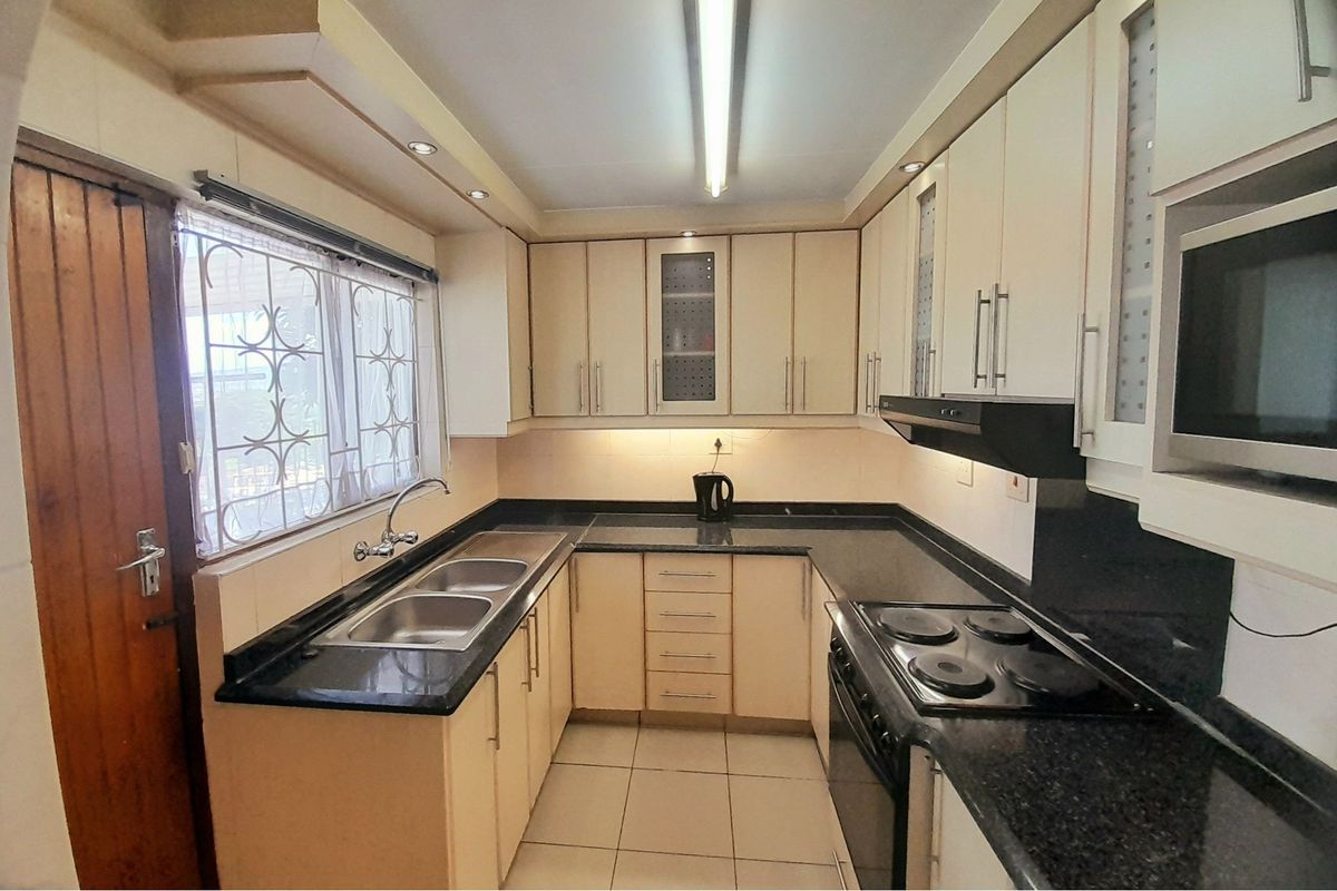 Functional kitchen featuring dark granite countertops, light-toned cabinetry, double stainless steel sink, and built-in electric hob with extractor fan.