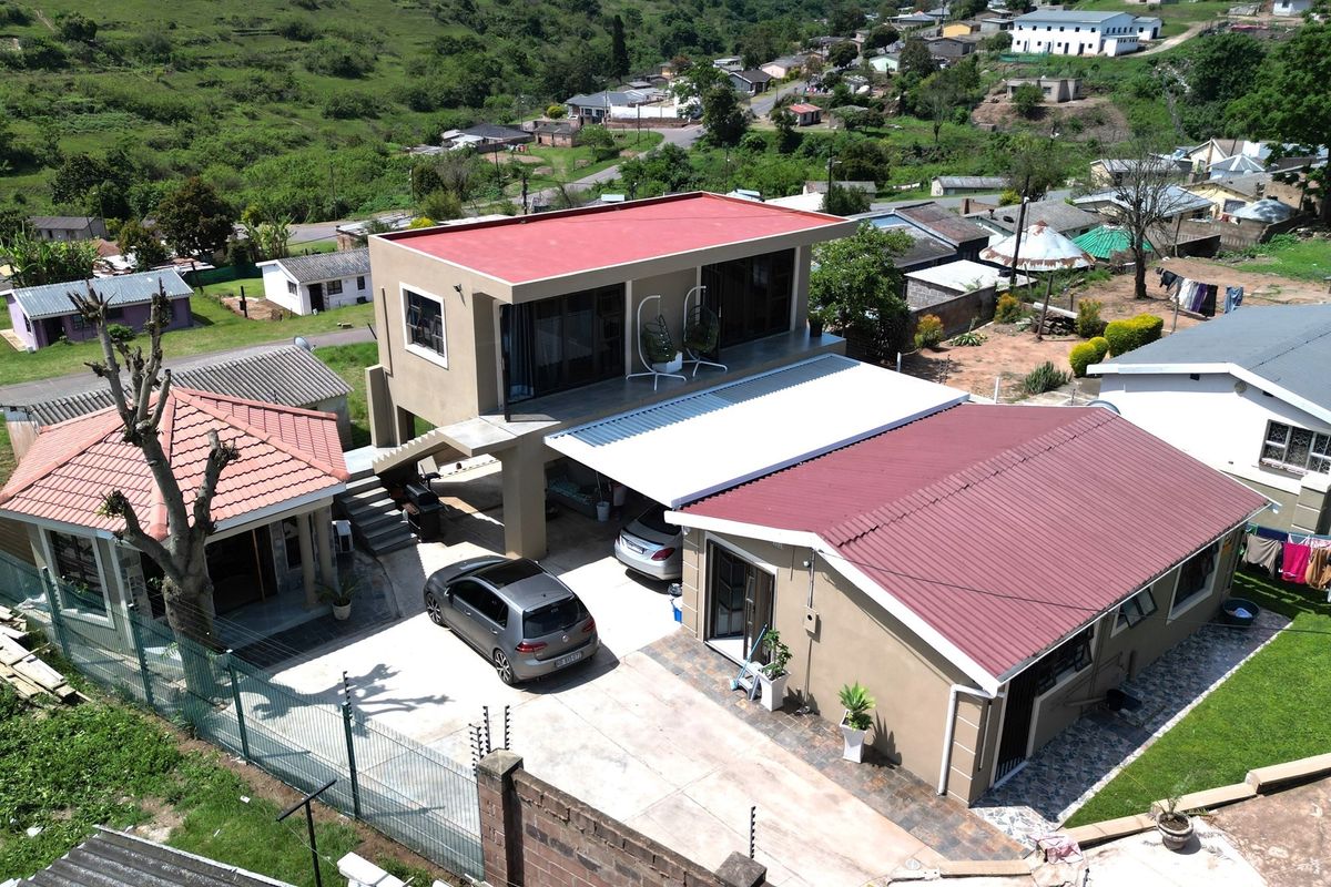 Aerial view of a multi-structure residential property featuring a two-story main house with a balcony, a separate outbuilding, and paved driveway area.