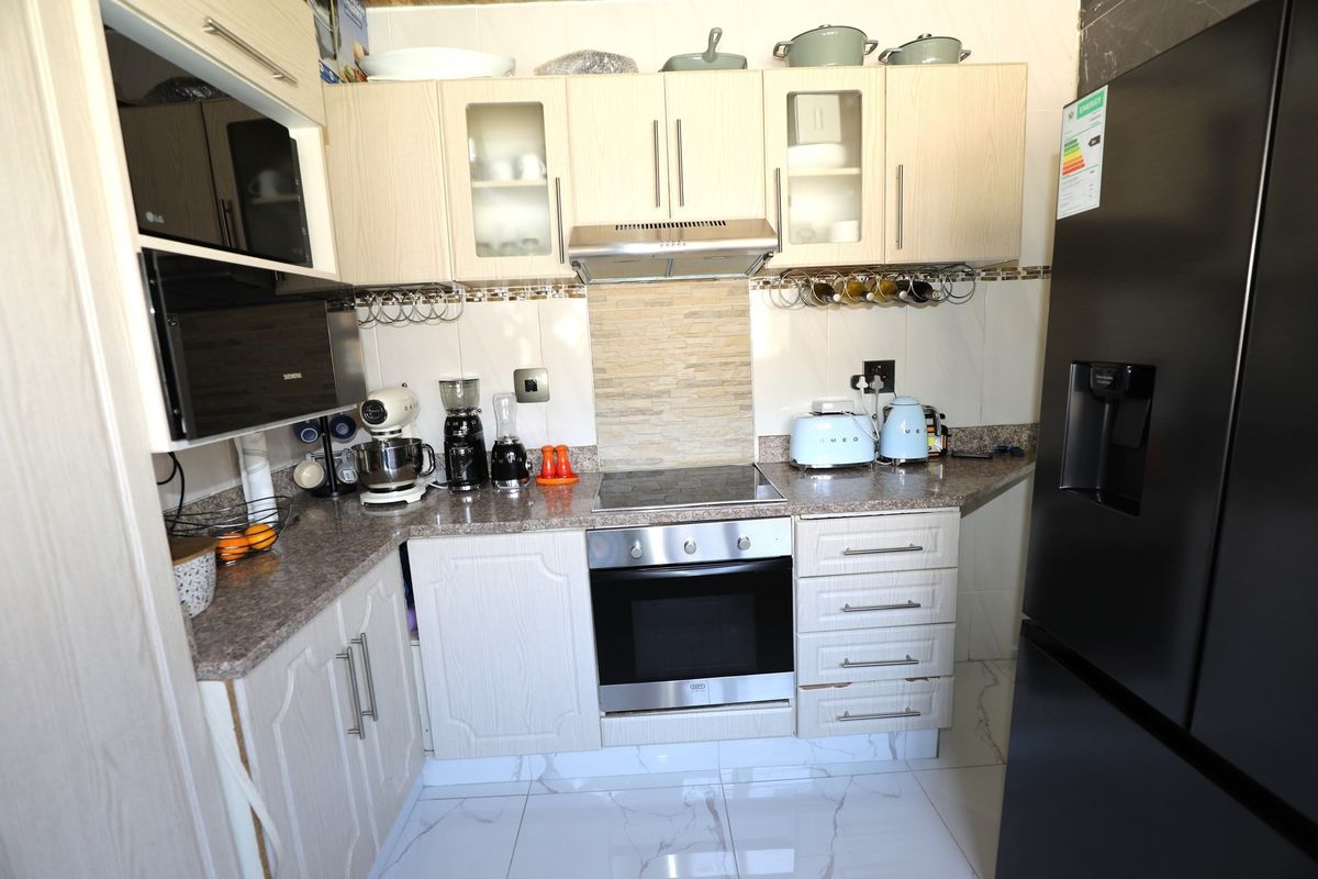 Compact kitchen featuring light wood-grain cabinetry, stone-look countertops, built-in oven, electric hob, extractor fan, and tiled flooring.