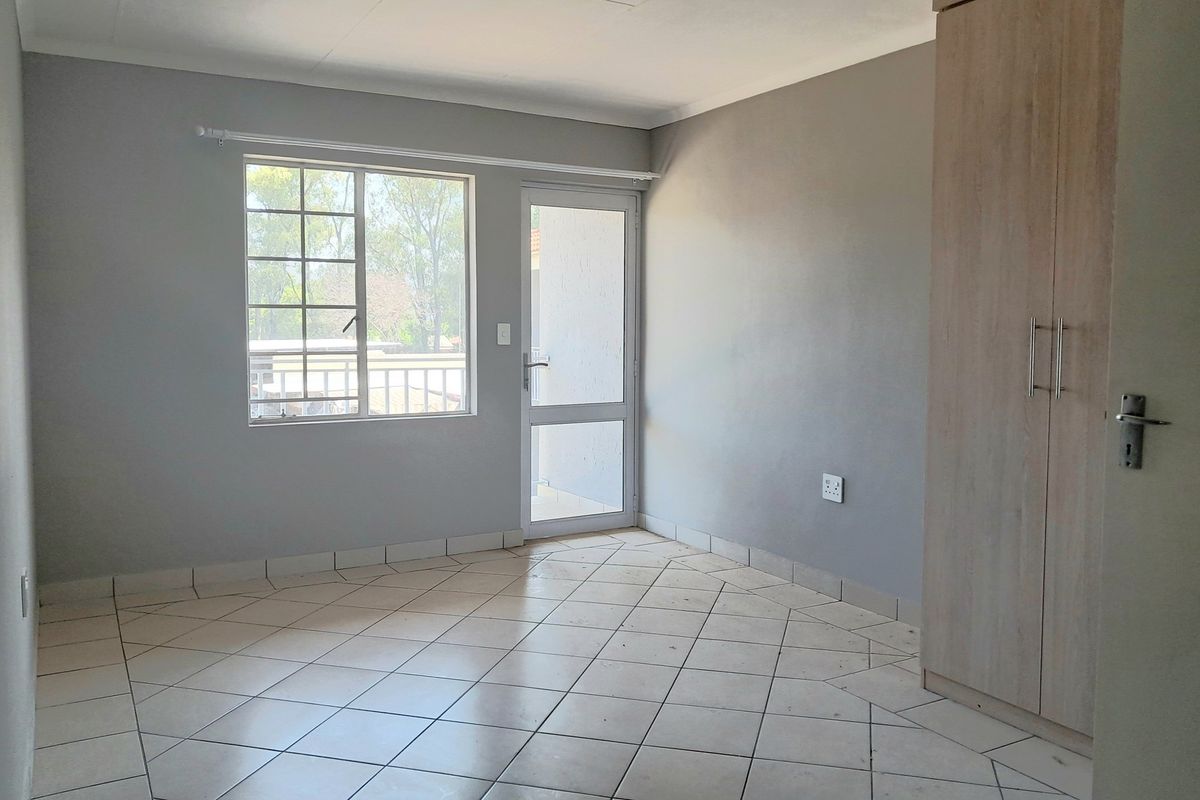 A neutral, empty bedroom featuring tiled flooring, a built-in wardrobe, and direct access to an outdoor area through a glass-paneled door.