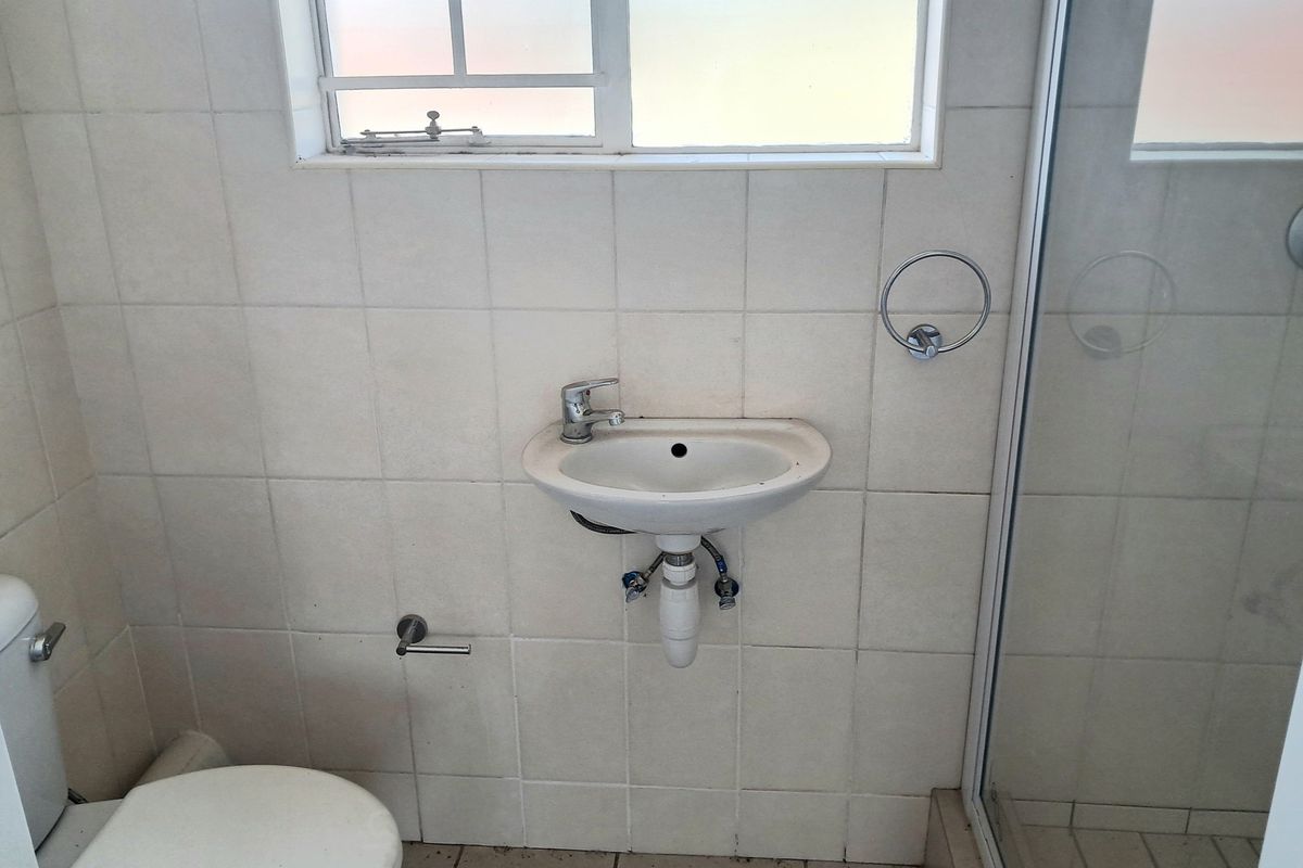 A functional bathroom featuring a wall-mounted basin, shower enclosure, and toilet, finished with neutral ceramic wall tiles.