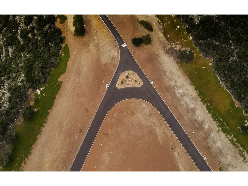 An aerial view of a Y-shaped asphalt road junction within a residential development, featuring a central landscaped traffic island.
