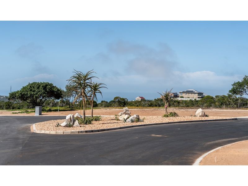 A view of a paved residential street with a landscaped traffic island featuring gravel, boulders, and indigenous plants in a well-maintained estate.