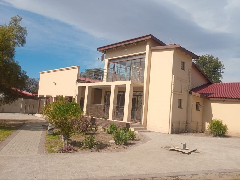 A two-story residential building featuring a balcony with metal railings, paved driveway, and landscaped garden area.