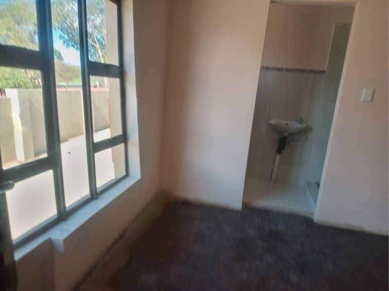 A bedroom featuring a large window and an en-suite bathroom area with a wall-mounted basin, currently in an unfinished state.
