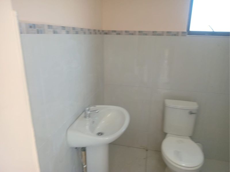A functional bathroom featuring a pedestal sink, a standard toilet, and neutral wall tiling with a decorative border.