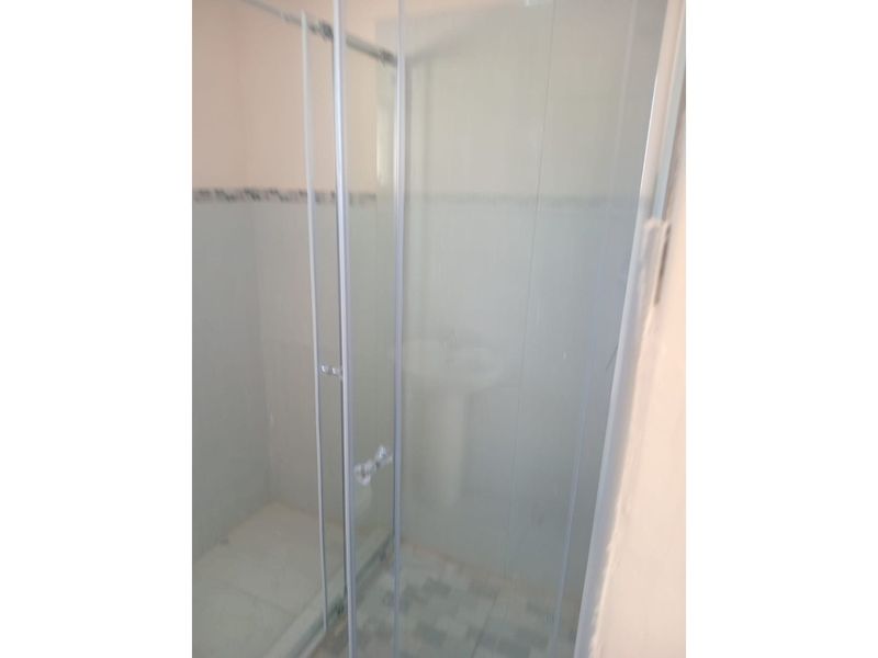 A functional bathroom featuring a glass-enclosed shower stall and a pedestal basin with tiled flooring.