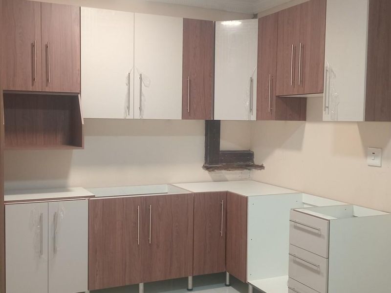 A kitchen area featuring two-tone wood and white cabinetry, currently in an unfinished state with missing countertops and exposed wall sections.