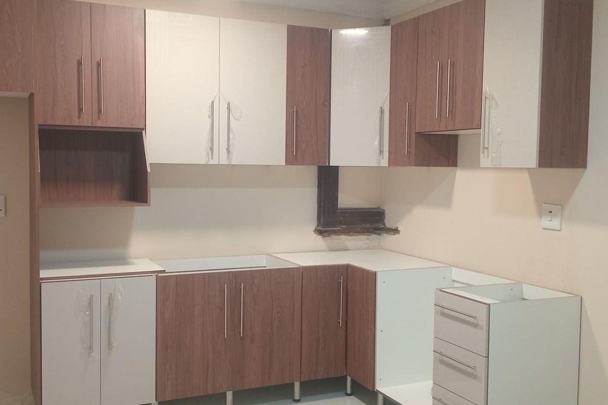 A kitchen area featuring two-tone wood and white cabinetry, currently in an unfinished state with missing countertops and exposed wall sections.