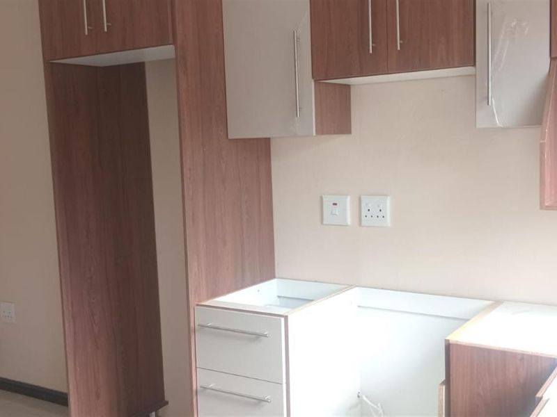 A compact kitchen area featuring wood-grain and white cabinetry with dedicated spaces for appliances and electrical outlets.