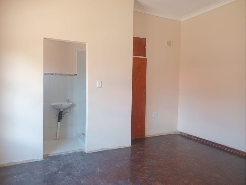An empty bedroom featuring a built-in cupboard and an en-suite bathroom area with a wall-mounted basin.