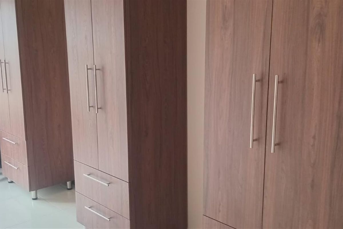 A bedroom featuring built-in wooden wardrobes with modern metal handles and tiled flooring.