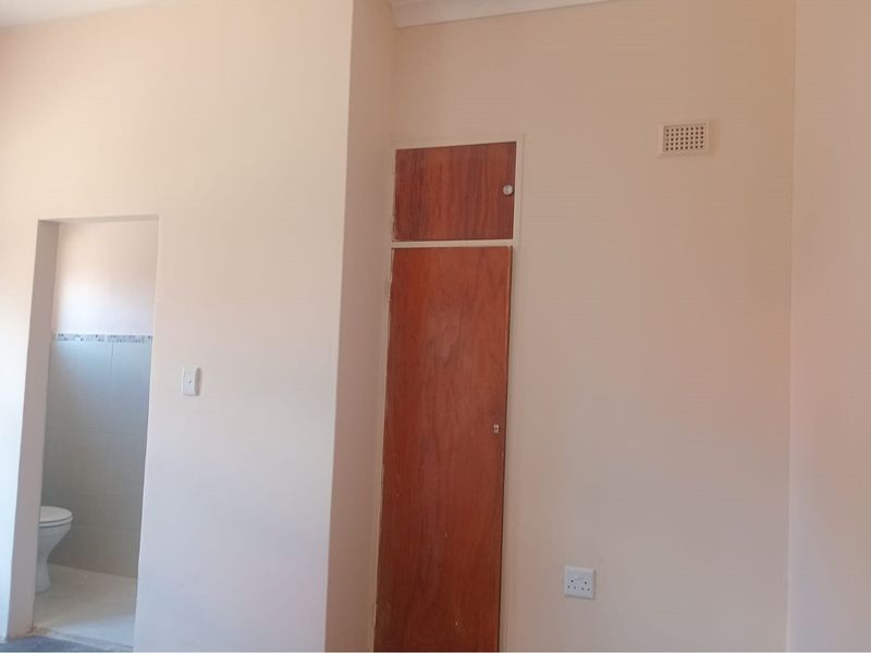 A bedroom interior featuring a built-in wooden cupboard and an adjacent doorway leading to a tiled bathroom area.