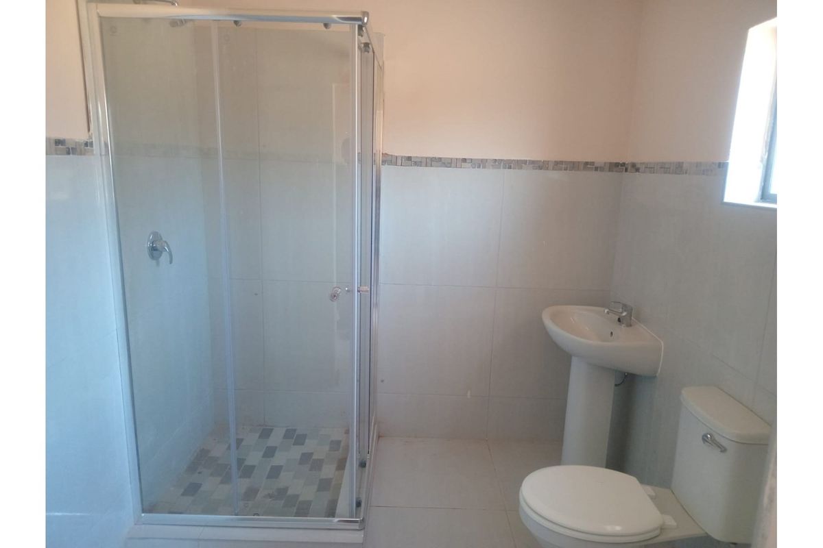 A functional bathroom featuring a glass-enclosed shower, pedestal basin, and toilet with neutral wall tiling and a decorative mosaic border.