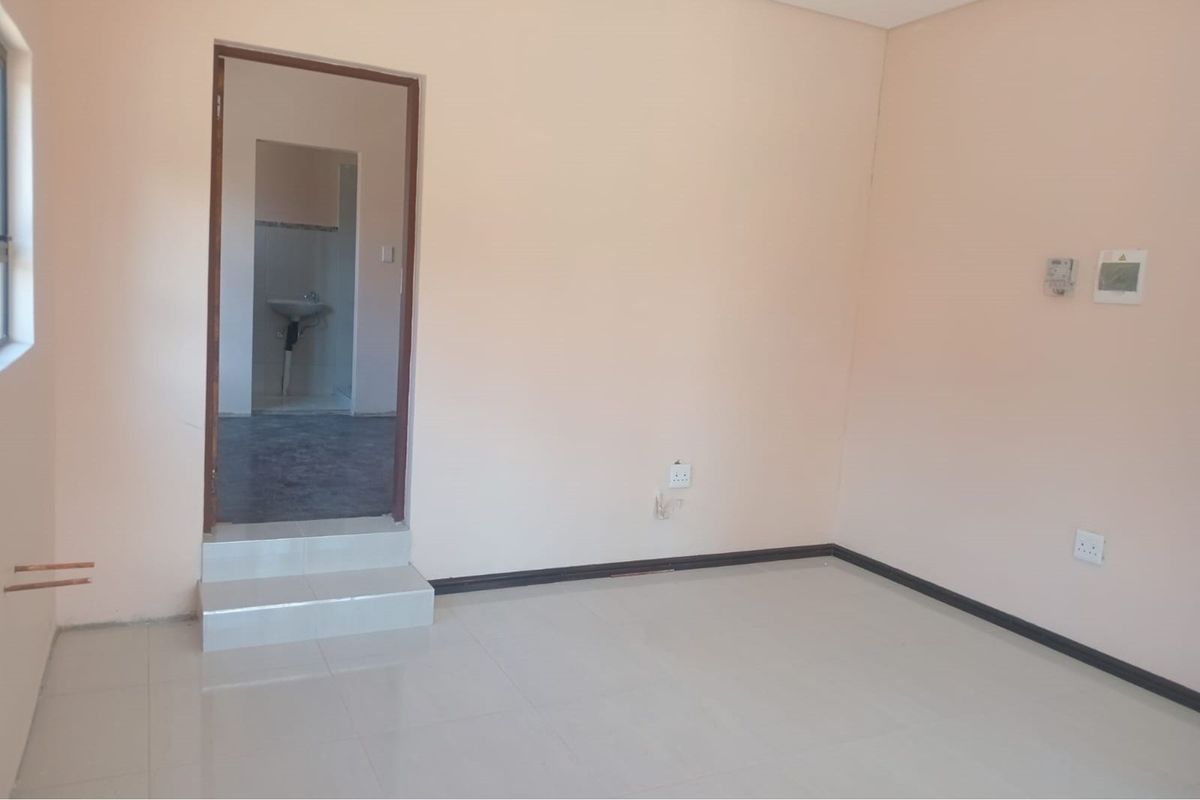 An empty living area featuring tiled flooring, a raised doorway leading to an adjacent space, and visible electrical points.