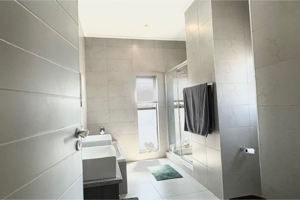 Modern bathroom featuring dual vessel sinks, a glass-enclosed shower, and neutral floor-to-ceiling tiling.
