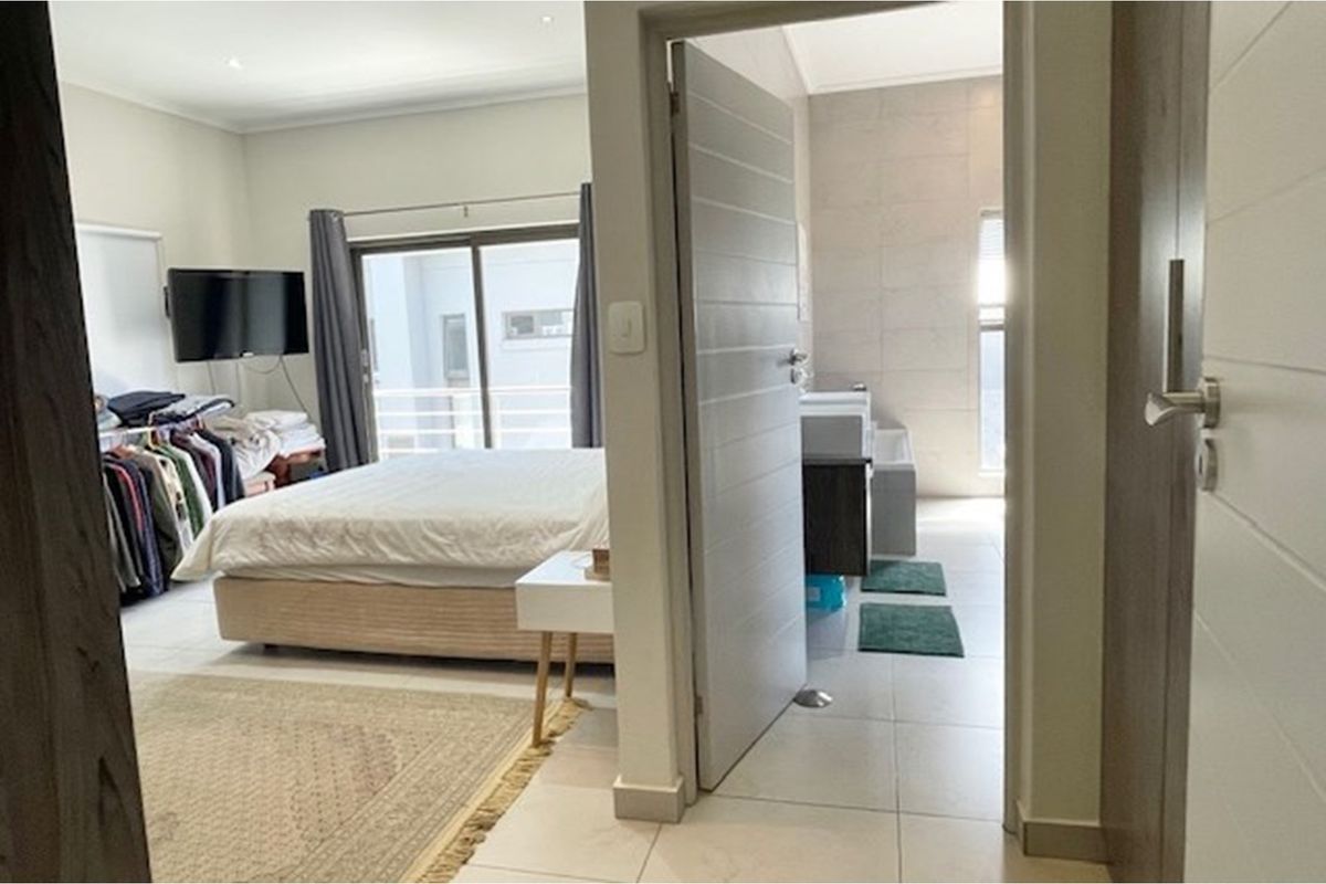 A spacious bedroom featuring tiled flooring, sliding glass doors leading to a balcony, and an adjoining en-suite bathroom.