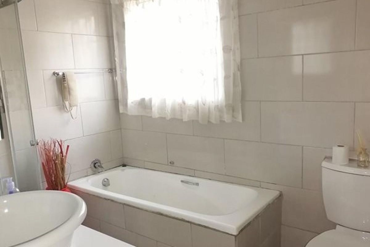 A functional bathroom featuring a built-in bathtub, wall-mounted basin, and toilet, finished with neutral wall tiling.