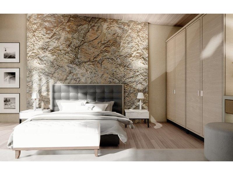 A modern bedroom featuring a textured stone accent wall, light wood flooring, and integrated floor-to-ceiling cabinetry.