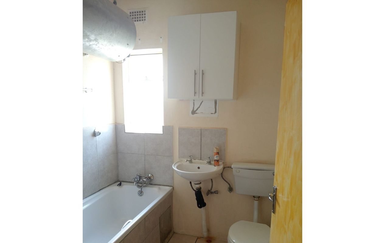 A compact bathroom featuring a standard bathtub, pedestal basin, and toilet, with an exposed water heater and wall-mounted storage cabinet.