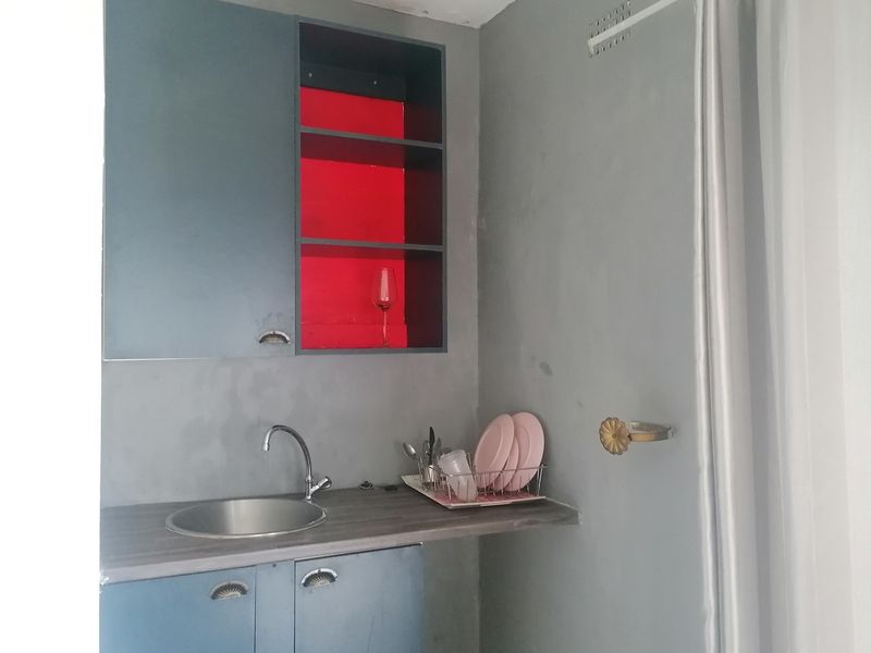 A compact scullery or kitchenette area featuring blue built-in cabinetry, a stainless steel sink, and a contrasting red open shelving unit.