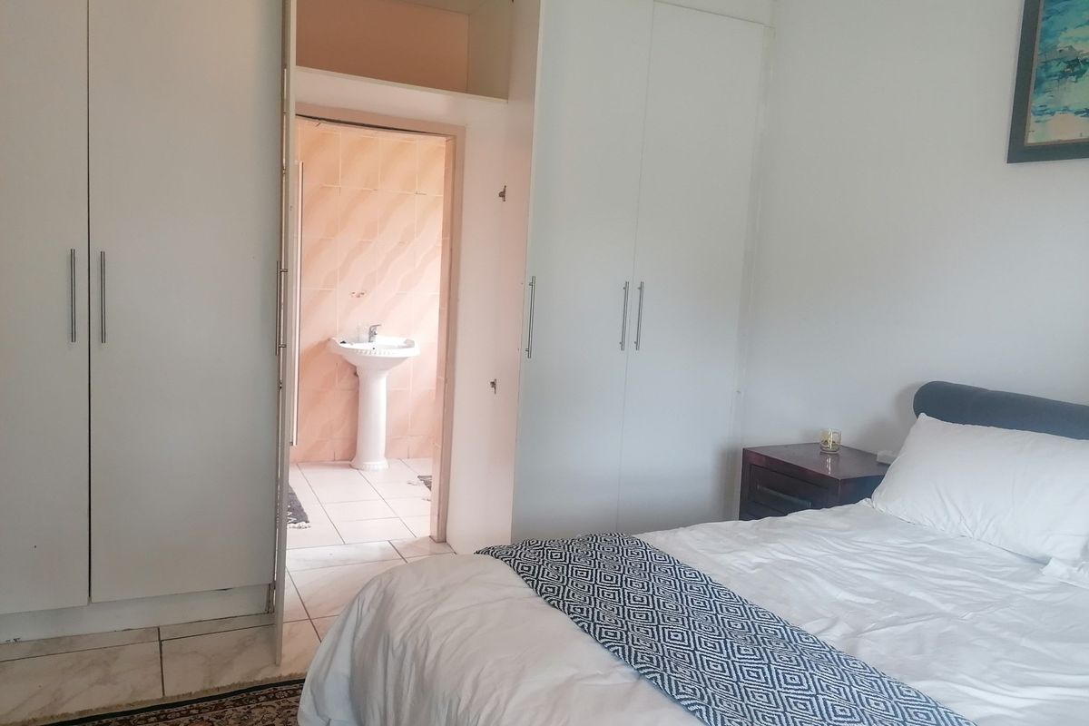 Bedroom featuring built-in cupboards and an en-suite bathroom with a pedestal basin and tiled finishes.