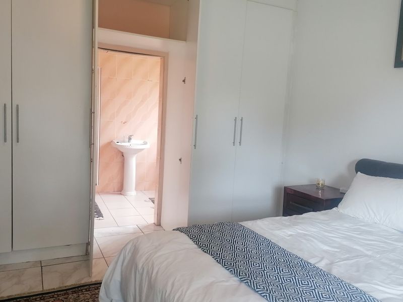 Bedroom featuring built-in cupboards and an en-suite bathroom with a pedestal basin and tiled finishes.