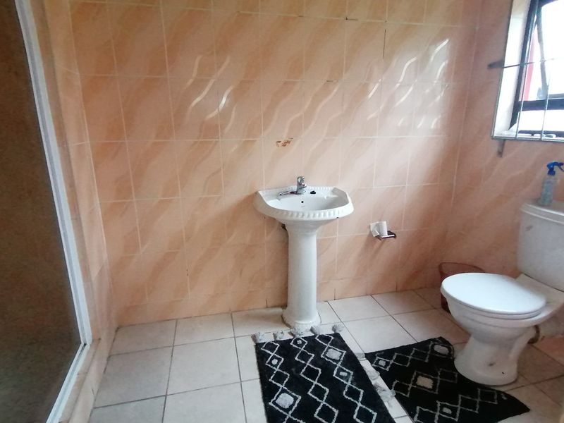 A functional bathroom featuring a pedestal sink, toilet, and shower enclosure with dated wall tiling and floor tiles.
