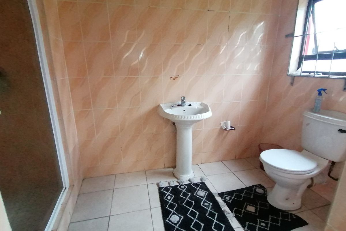 A functional bathroom featuring a pedestal sink, toilet, and shower enclosure with dated wall tiling and floor tiles.
