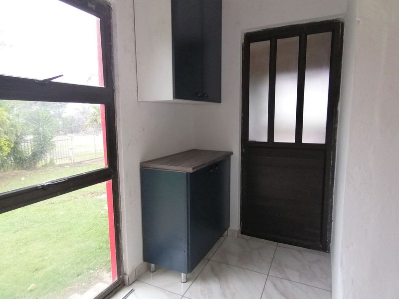 A compact scullery or utility area featuring built-in cabinetry, tiled flooring, and direct access to the garden through a glass-paneled door.